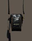 Black crocodile-patterned handbag with a tassel on a peach background